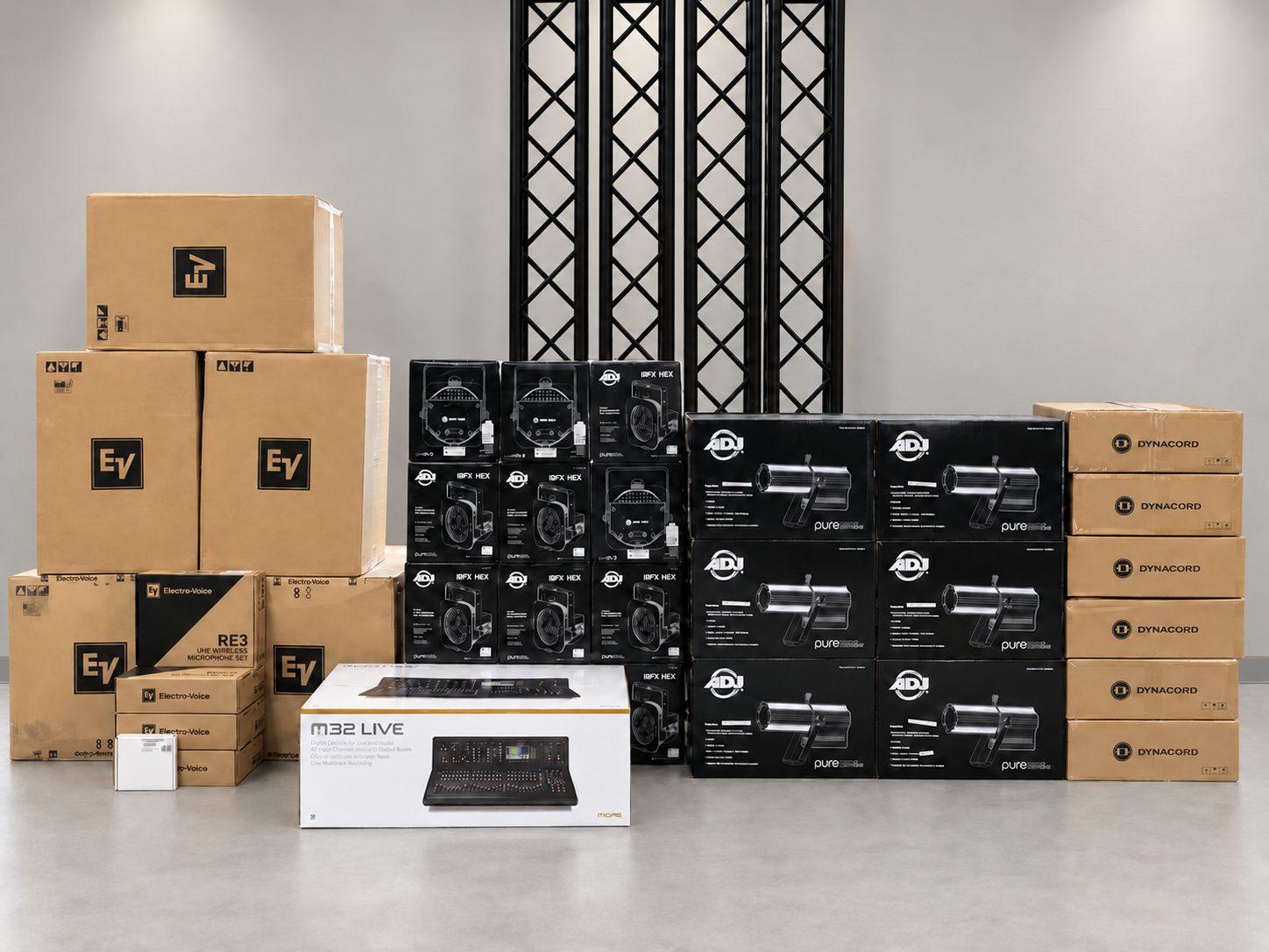 Boxed audio and lighting equipment with black truss against a light gray wall